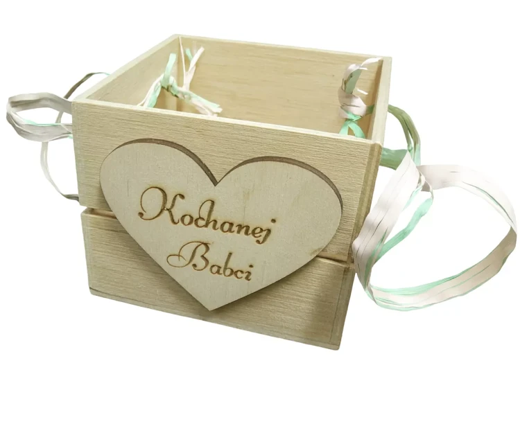 Drewniane pudełko z napisem „Kochanej Babci”, ozdobione wstążkami po bokach. Rustykalny styl i serduszkowa plakietka nadają mu ciepły, osobisty charakter. Idealny jako prezent na Dzień Babci lub inną wyjątkową okazję.