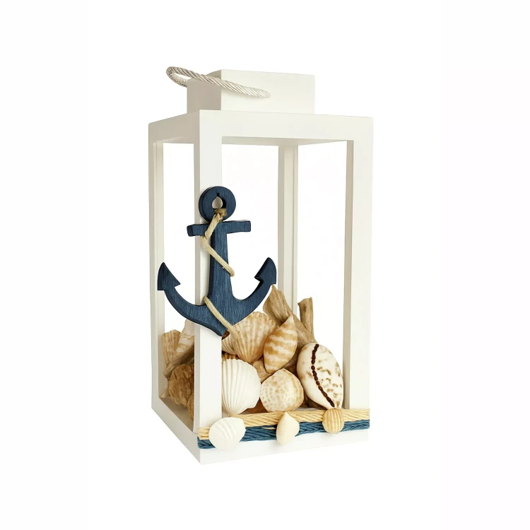 Biały lampion z uchwytem ze sznurka, ozdobiony granatową kotwicą i muszelkami. Wewnątrz dekoracja z muszli, na dole pasek z niebiesko-beżowego sznurka. Styl marynistyczny, idealny do nadmorskich aranżacji.