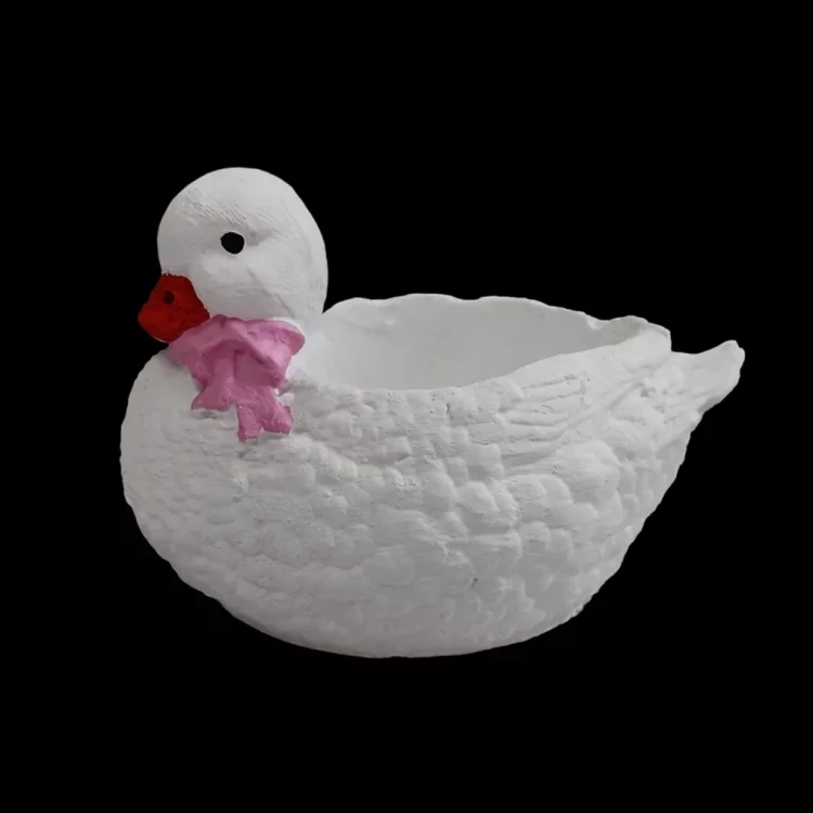 Biała gipsowa kaczka Maja z różową kokardką na szyi, z fakturą piór i otwartym wnętrzem na drobne dekoracje, przedstawiona na czarnym tle.