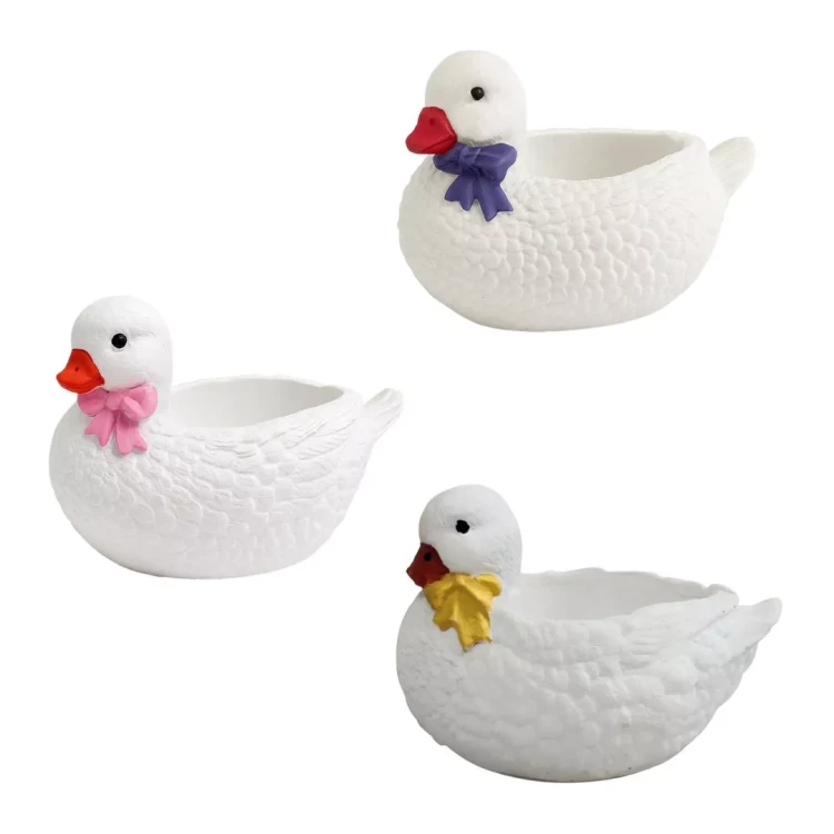 Gipsowe kaczki dekoracyjne z fakturą piór i kokardkami w trzech kolorach: żółtym, różowym i fioletowym, z otworami na drobne rośliny lub ozdoby.
