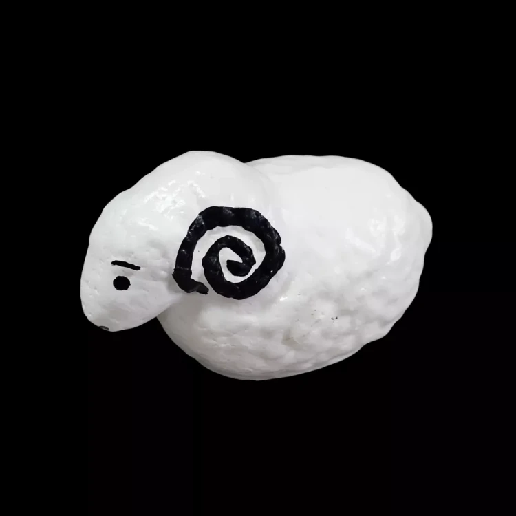 Biała, minimalistyczna figurka baranka o chropowatej fakturze, z czarnym okiem i spiralnym rogiem, ustawiona na czarnym tle, które podkreśla jej kształt i kontrast.