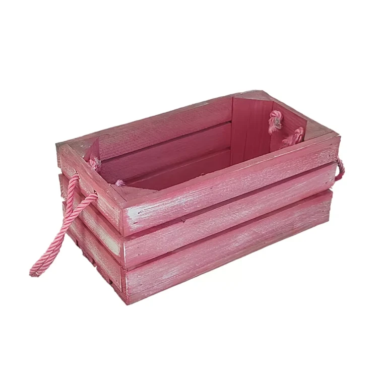 Postarzana różowa skrzynka z drewnianych listewek i sznurkowymi uchwytami, widoczna w ujęciu frontalnym.