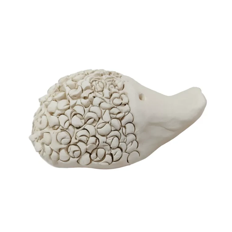 Ceramiczna figurka jeża z gładkim pyszczkiem i dwoma małymi otworami jako oczy, a całe ciało pokryte licznymi spiralnymi elementami imitującymi kolce, ustawiona na jasnym tle.