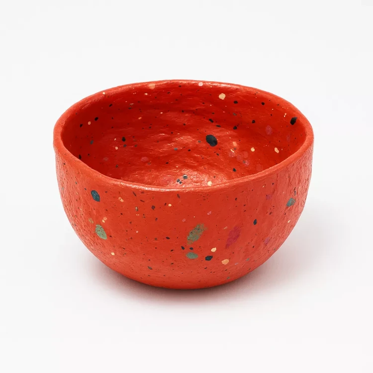 Czerwona ceramiczna miska z kolorowymi, nieregularnymi kroplami dekoracyjnymi na białym tle.
