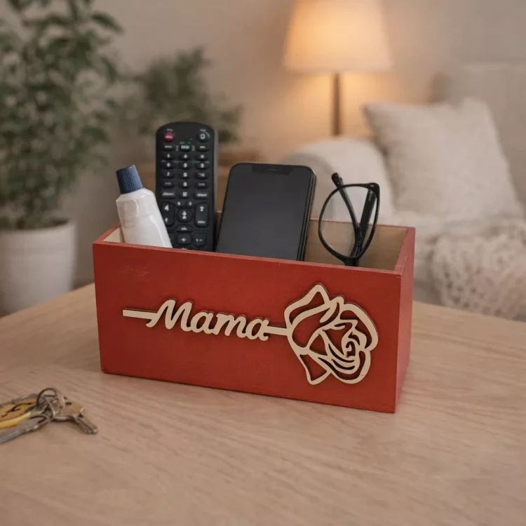 Czerwona drewniana skrzynka organizer z napisem „Mama” i motywem róży, wypełniona drobnymi akcesoriami domowymi, ustawiona na stole w przytulnym salonie.