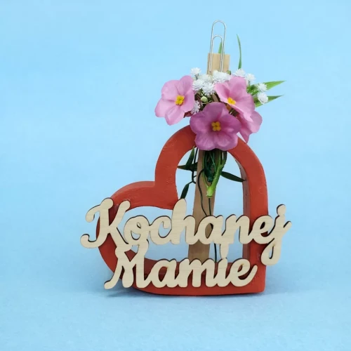 Serce z czerwonej ramki z napisem „Kochanej Mamie”, w środku przypięty klamerką mały bukiecik różowych i białych sztucznych kwiatów na jasnoniebieskim tle.