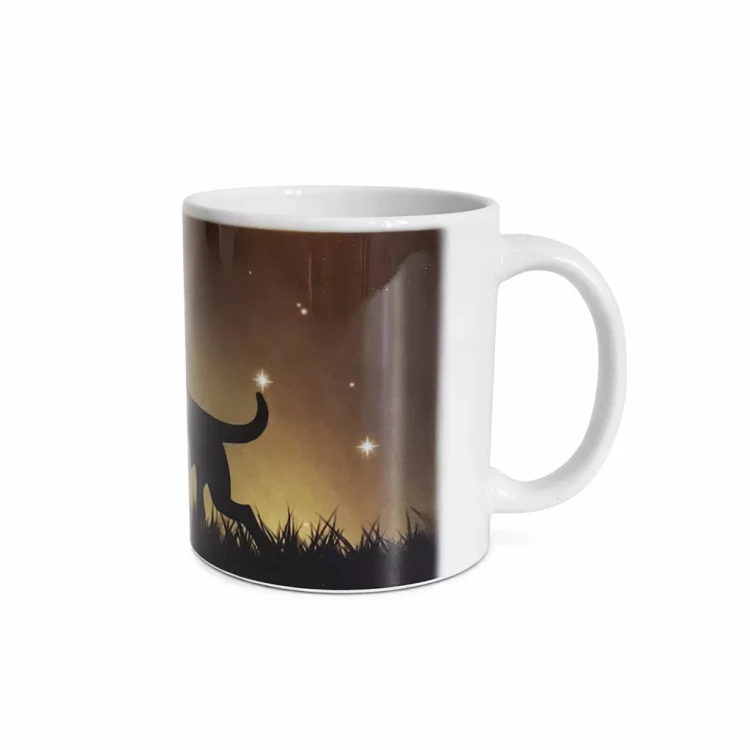 Kubek z białym uchem i wnętrzem, na zewnętrznej stronie grafika ogon czarnego psa idącego po trawie na tle nocnego nieba w ciepłych odcieniach brązu i żółci z widocznymi gwiazdami.