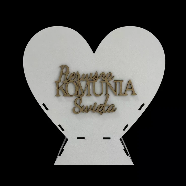 Białe serce dekoracyjne na czarnym tle, z drewnianym, wypukłym napisem „Pierwsza Komunia Święta”. Prosty, elegancki element pamiątkowy lub ozdoba stołu na uroczystość komunijną.