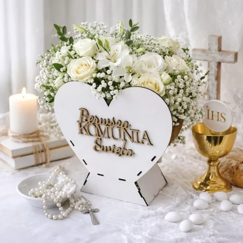 Kompozycja komunijna z białymi kwiatami, świecą, różańcem, kielichem z Hostią IHS, drewnianym napisem „Pierwsza Komunia Święta”, krzyżem i migdałami na białej koronce.