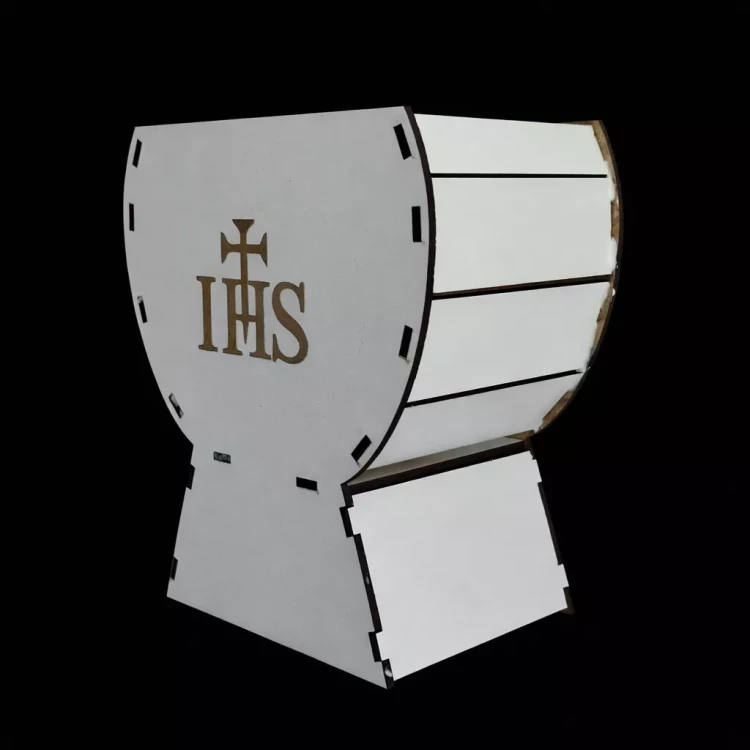 Biała, segmentowa osłonka w formie kielicha liturgicznego z wyciętych paneli, na froncie symbol „IHS” z krzyżem. Gładka, matowa powierzchnia, wyraźne łączenia elementów, całość na czarnym tle, dobrze widoczny kształt i detale.