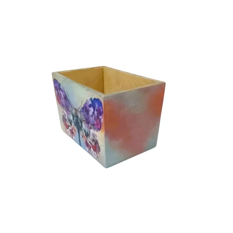 Drewniana skrzyneczka z otwartą górą, z zewnątrz pomalowana w intensywne kolory. Na jednej stronie widoczny motyl w odcieniach fioletu, niebieskiego i czerwieni, druga strona ma płynne przejścia barw. Wnętrze surowe, jasne drewno.