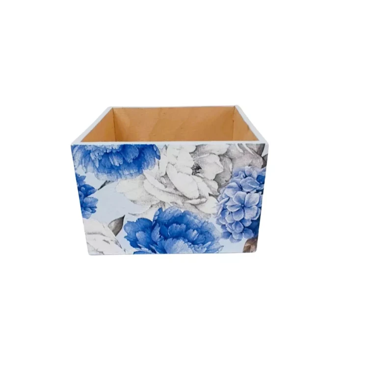 Kwadratowy pojemnik z drewna, zewnętrznie ozdobiony wyrazistymi niebiesko białymi kwiatami. W środku widoczne surowe drewno, bez dodatkowych dekoracji.
