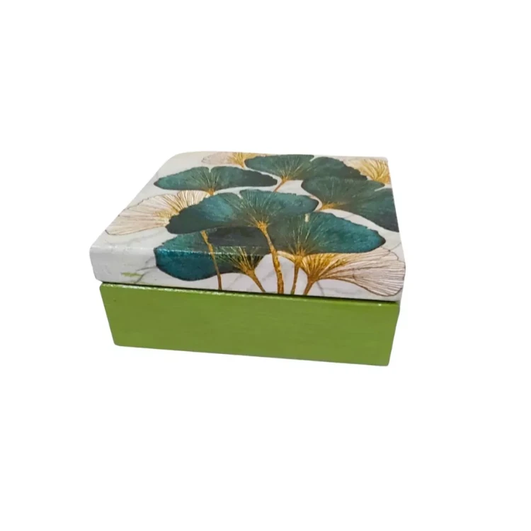 Kwadratowe drewniane pudełko z zieloną podstawą i białą pokrywką ozdobioną zielono‑złotymi liśćmi o delikatnych złotych żyłkach, tworzącymi elegancki roślinny wzór.