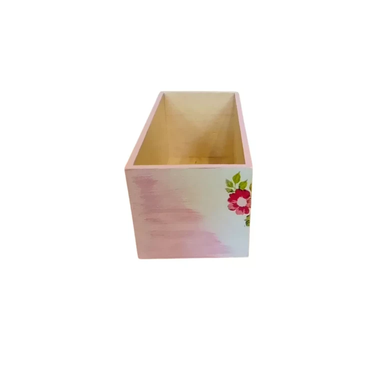 Prostokątna drewniana skrzynka bez wieka, pomalowana na jasny róż i biel. Jej boczna ścianka jest ozdobiona motywem różowych i czerwonych kwiatów z zielonymi liśćmi wykonanym techniką decoupage.