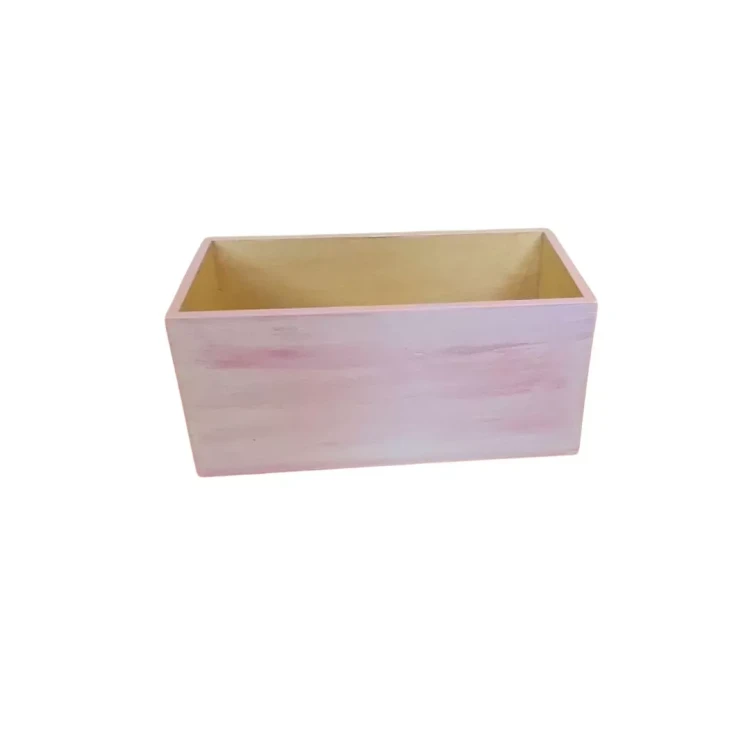 Drewniane pudełko w kształcie prostokąta, z otwartą górą. Zewnętrzne ścianki pomalowane na jasny róż z widocznymi pociągnięciami pędzla, wnętrze w naturalnym kolorze drewna. Gładkie krawędzie i prosta, minimalistyczna forma.