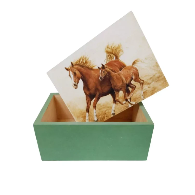 Drewniane pudełko z zieloną podstawą i wieczkiem z ilustracją dwóch pędzących koni. Pokrywka lekko odsunięta, widać jasne, surowe wnętrze. Kontrast między malowaną bazą a dekoracyjnym motywem na wieczku.