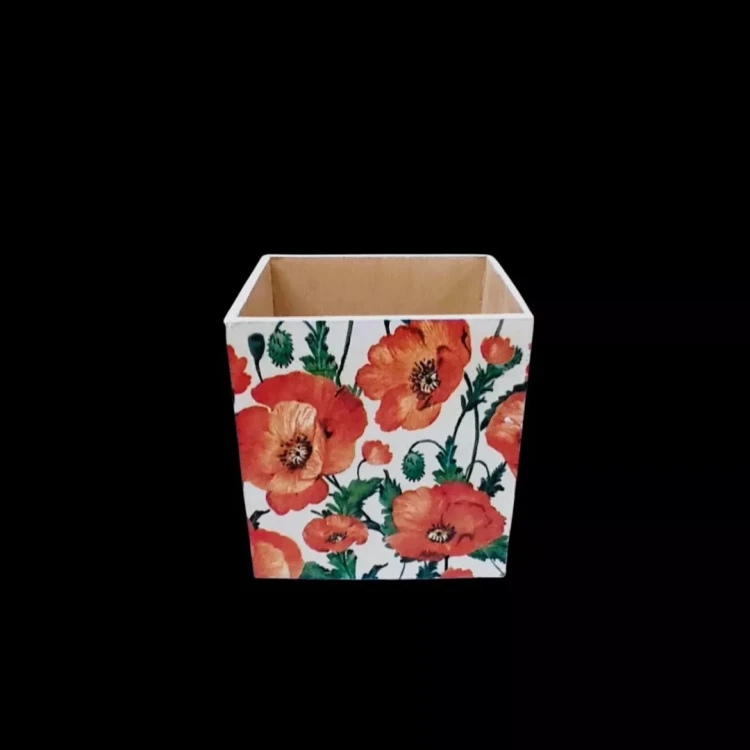 Kwadratowy pojemnik ozdobiony techniką decoupage. Na białych ściankach widnieją gęsto rozmieszczone, ilustrowane maki w odcieniach czerwieni i pomarańczu. Widoczne zielone łodygi i pąki kwiatów. Wnętrze jest jasne, drewniane.