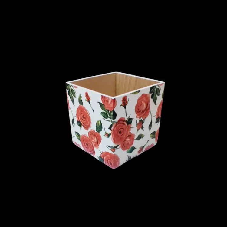 Kwadratowe pudełko drewniane, decoupage. Motyw: czerwone róże na białym tle. Wnętrze: naturalne drewno.  Brak wieczka, otwarta góra. Wyraźny kontrast kolorystyczny między białą obudową a ciemnym tłem.