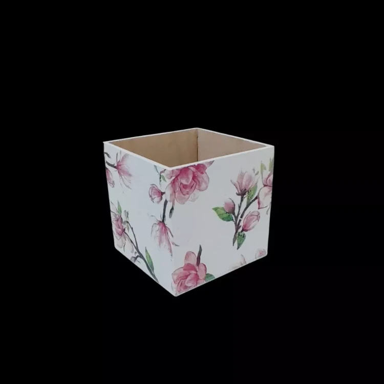 Elegancki drewniany pojemnik w kształcie sześcianu bez wieczka. Zewnętrzne boki pomalowane na biało z delikatnym, malarskim motywem magnolii w odcieniach różu i zieleni. Estetyczne rękodzieło w stylu romantycznym lub shabby chic.
