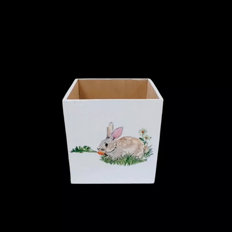 Ozdobny biały organizer z drewna o kształcie sześcianu bez wieczka. Zdobienia przedstawiają królika zjadającego marchewkę i polną roślinność. Styl decoupage.