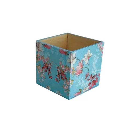 Kwadratowe pudełko z jasnego drewna, ozdobione techniką decoupage. Na zewnętrznych ściankach widoczny wzór gałązek wiśni z różowymi i białymi kwiatami na błękitnym tle.