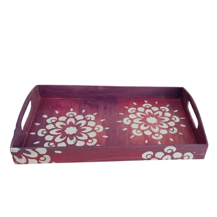 Widok z boku na fioletową, drewnianą tacę decoupage. Na jej dnie znajdują się dwie duże, białe mandale, a na przedniej ściance fragmenty białego, roślinnego wzoru. Taca ma wycięte podłużne uchwyty po bokach.