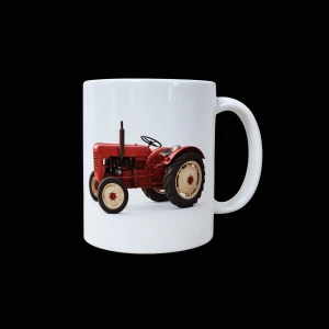 Biały ceramiczny kubek z nadrukiem czerwonego zabytkowego ciągnika rolniczego widocznego z boku. Traktor ma jasne felgi, duże tylne koło i charakterystyczną pionową rurę wydechową. Kubek pokazano na czarnym tle, z uchem po prawej stronie.
